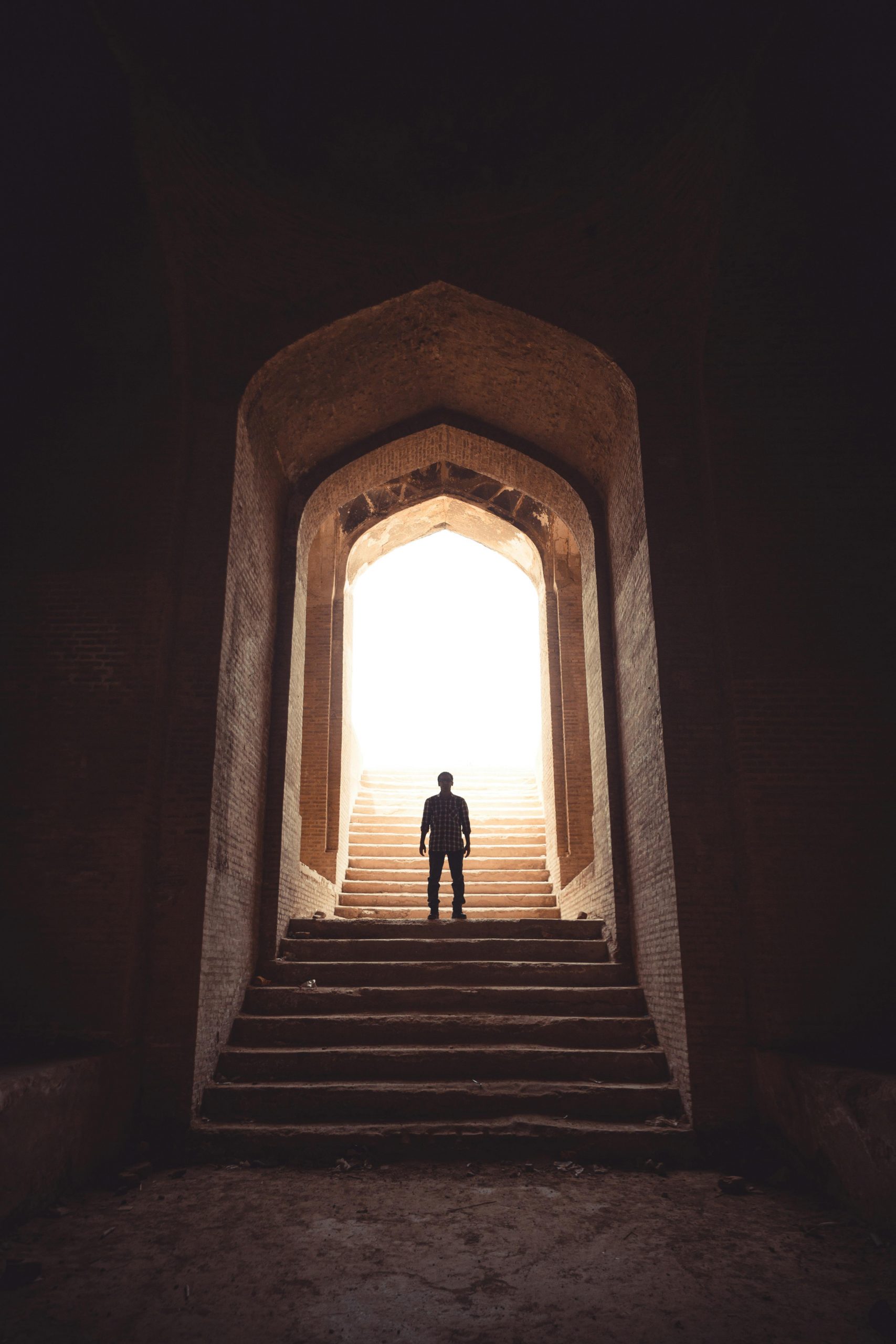 A solitary figure stands in a dramatic archway with steps leading to daylight.